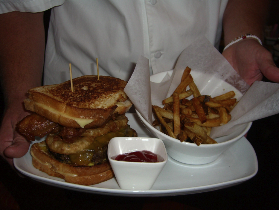 John Howie Steak's Kiss Your Hips Goodbye Burger, newly christened as the end result of  a renaming contest which drew over 4,000 submissions, some from as far away as Australia. The burger's original handle? The Triple Bypass Burger. Oh, and yes, this is a burger topped with breaded, deep-fried bacon and onion rings, and bookended between two grilled cheese sandwiches.